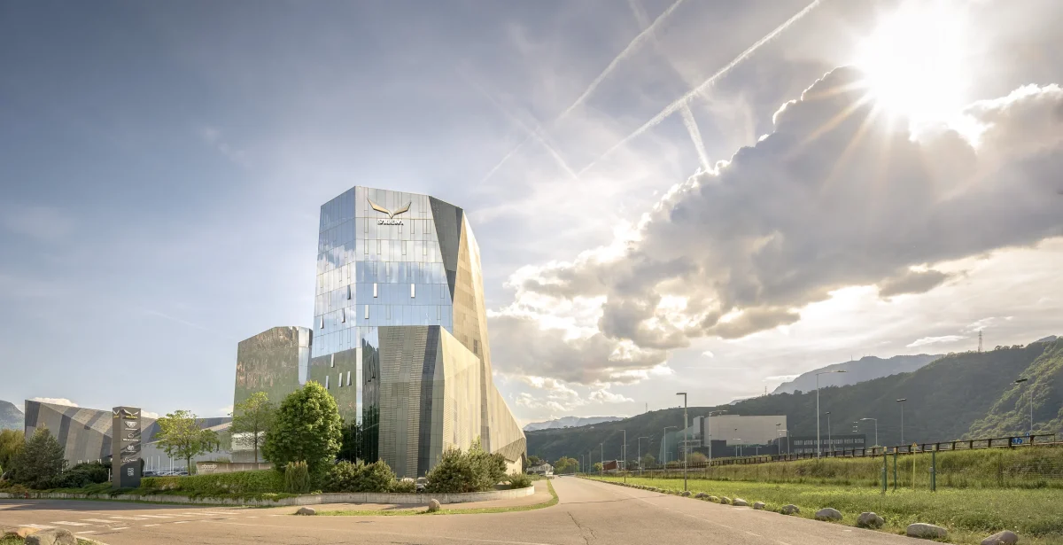 Sede centrale di Salewa, negozio sportivo altoatesino. Palazzo in vetro, che riflette la luce solare proveniente da ovest. Pomeriggio di giorno soleggiato. sulla destra l'autostrada