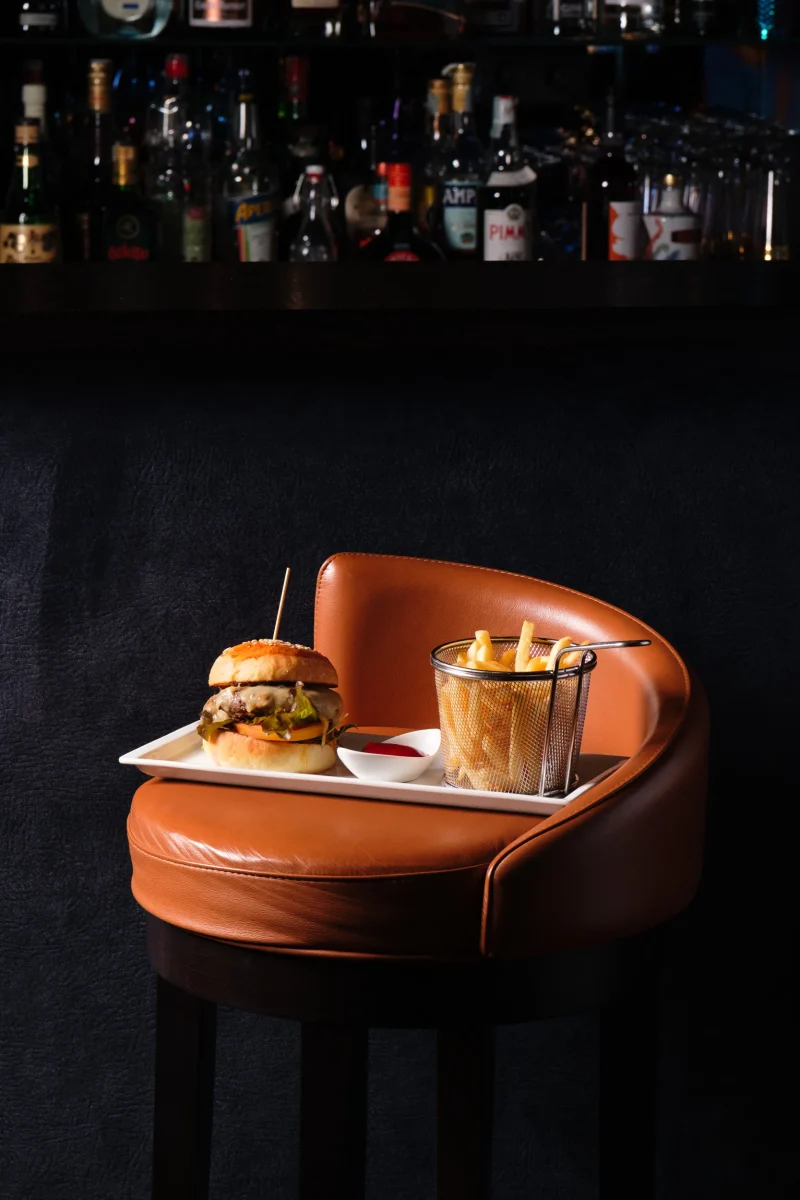 Hamburge e patatine su piatto appoggiato su sgabello da bar in pelle marrone - fotografo ristorante food alto adige