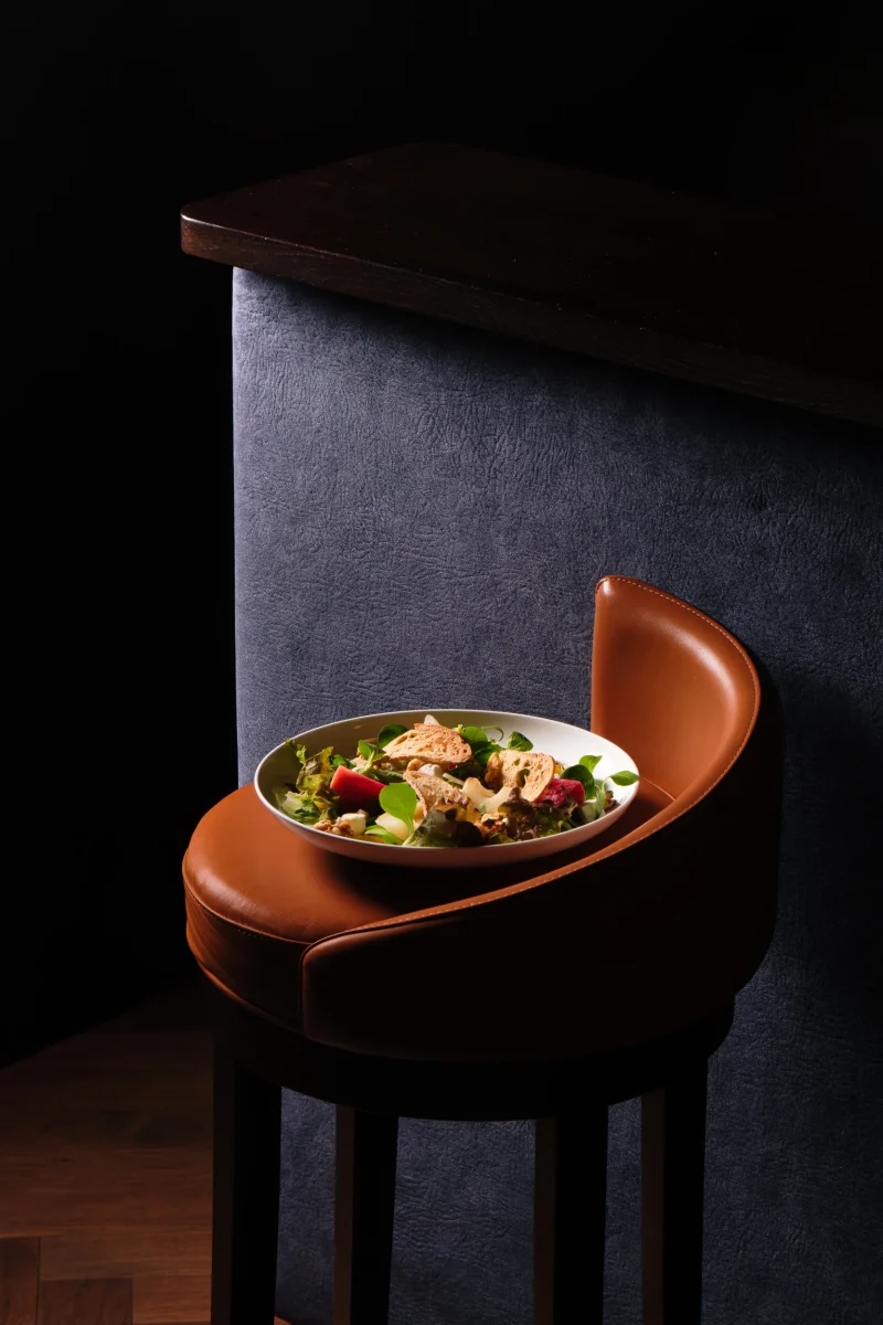 Piatto di insalata mista con crostini di pane su sgabello elegante in pelle da bar - fotografo ristorante stellato alto adige