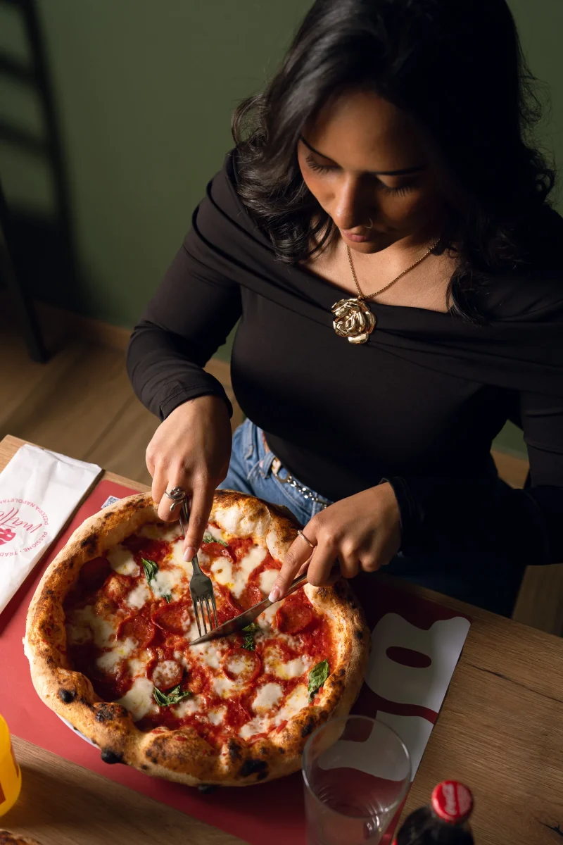 Ragazza che taglia pizza napoletana con illuminazione da flash da studio